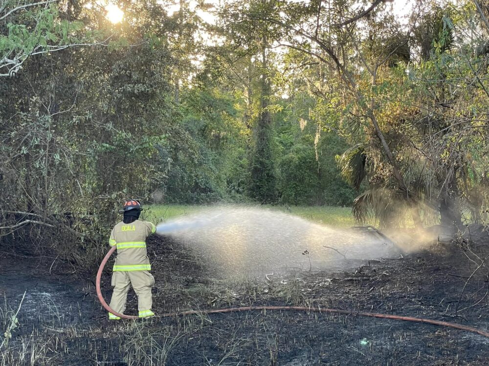 Ocala Fire Rescue grass fire near Cala Hills on March 24 2023 - photo of firefighter spraying water from hose