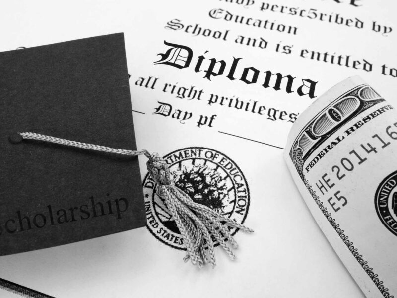 Diploma and graduation cap next to cash money