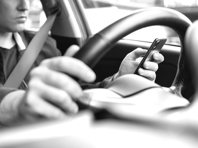 Texting and driving a car. Using mobile phone in traffic. Distracted driver, accident or crash. Irresponsible man typing sms text message with cellphone in city road or highway. Steering wheel.